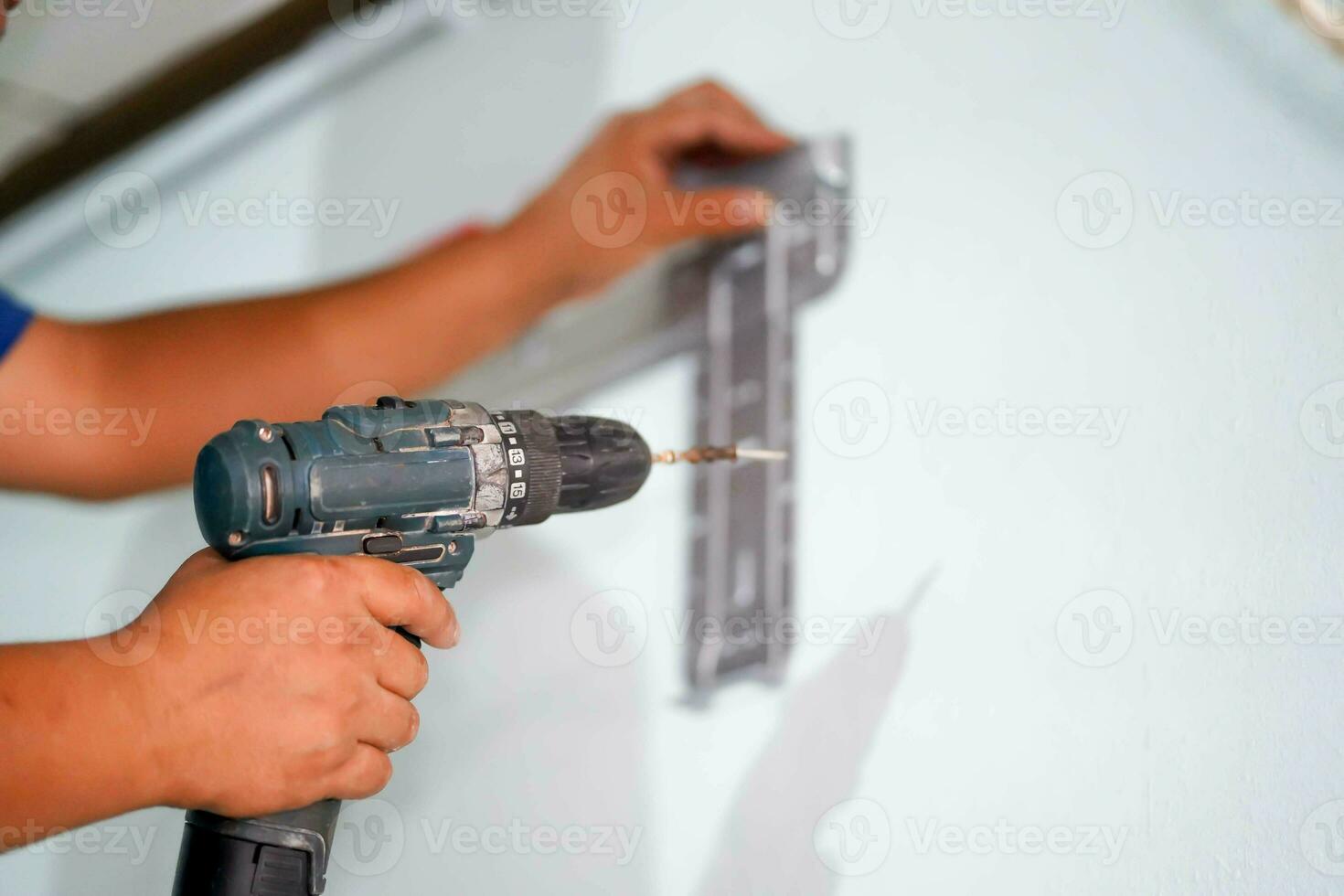 de cerca manos de constructor participación un eléctrico perforar es perforación un agujero en el pared para Instalar en pc aire condición a construcción sitio. foto
