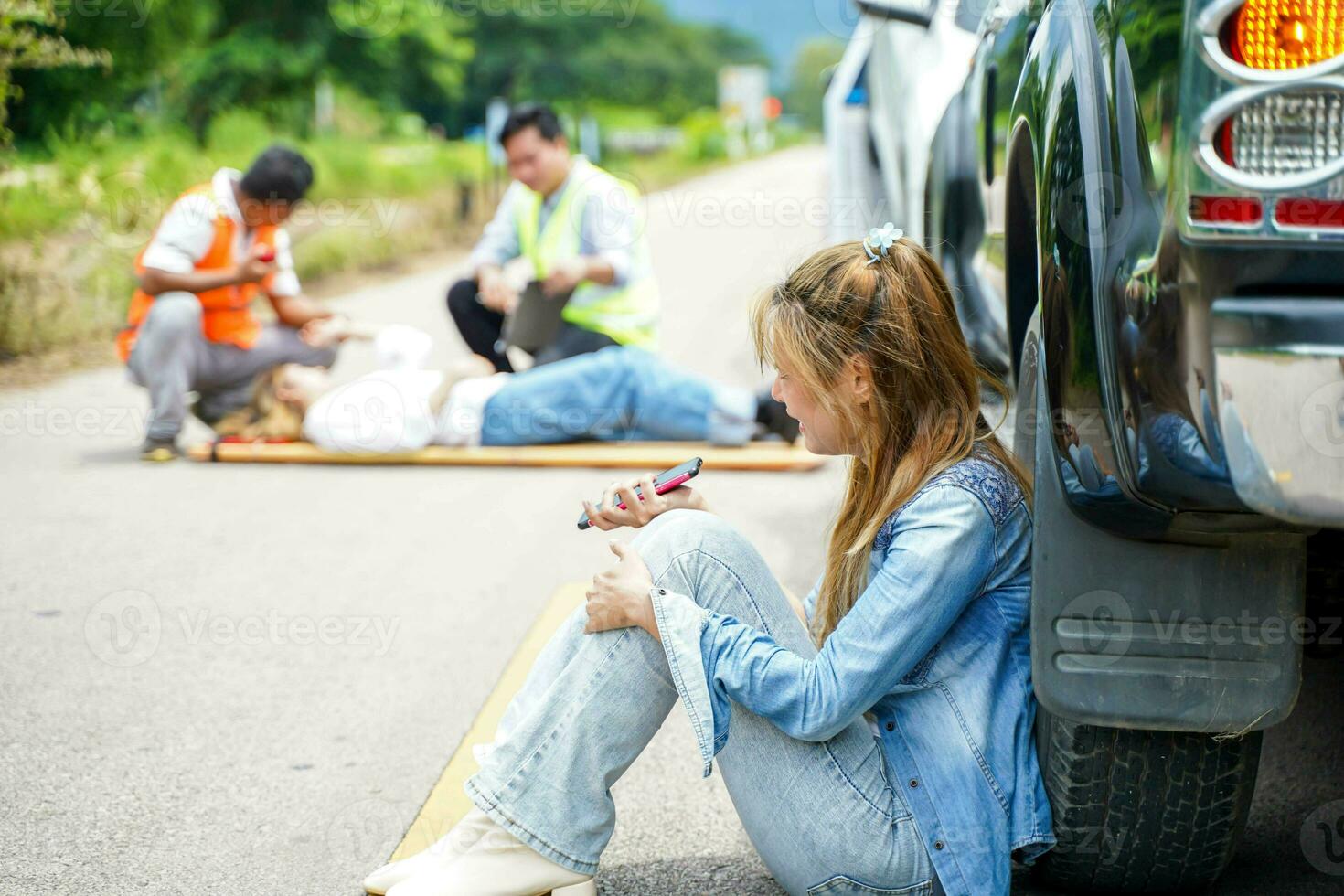 A young woman sits crying next to the car she crashed into someone on the road. photo