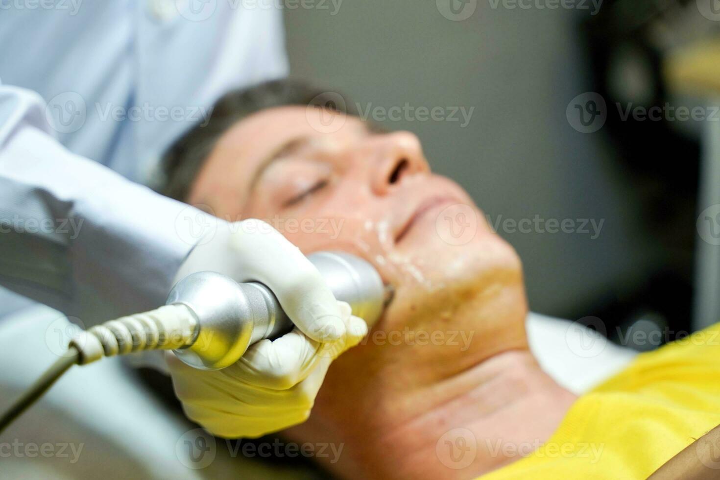 Closeup handsome man having therapy to stimulate facial skin and facial ultrasonic skincare treatment by professional cosmetologist wellbeing. photo