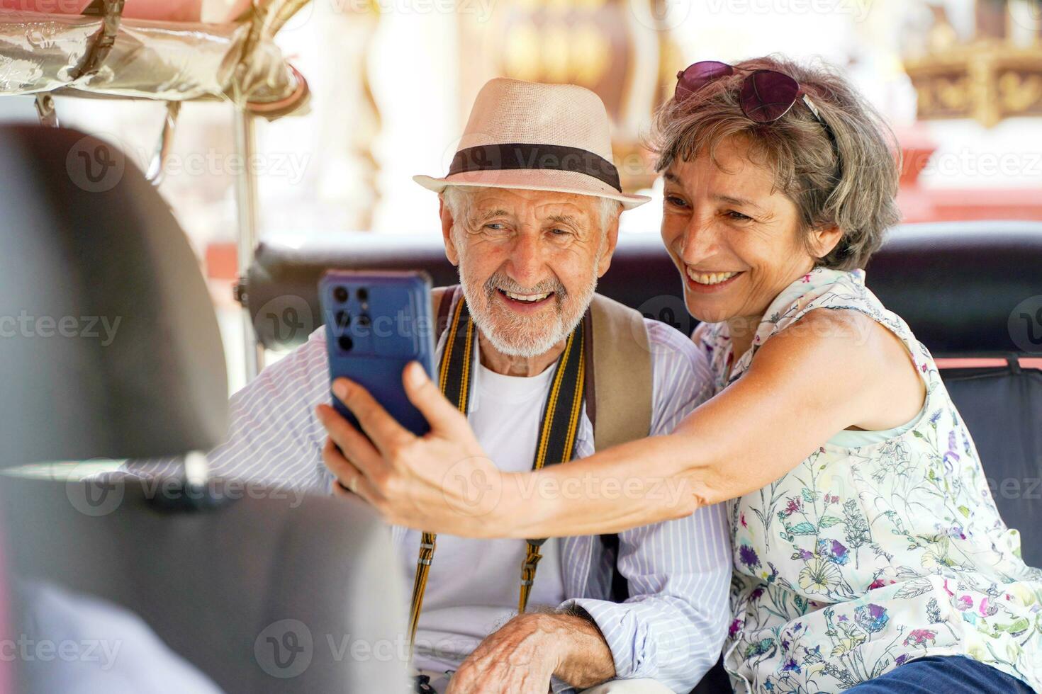 Closeup American senior tourist man with his friend European take a photo selfie in a Tuktuk Thailand taxi on blurred of city and sun bright background. Senior tourist concept