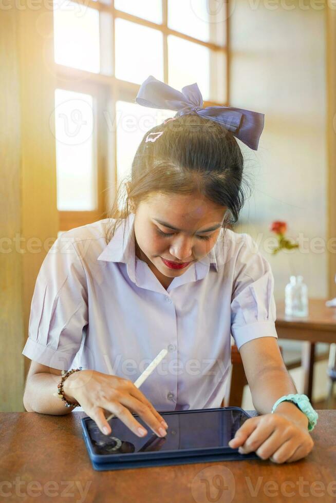 Closeup front view of Thai girl student using and study on tablet at school with sun flare background. Education studying concept. photo