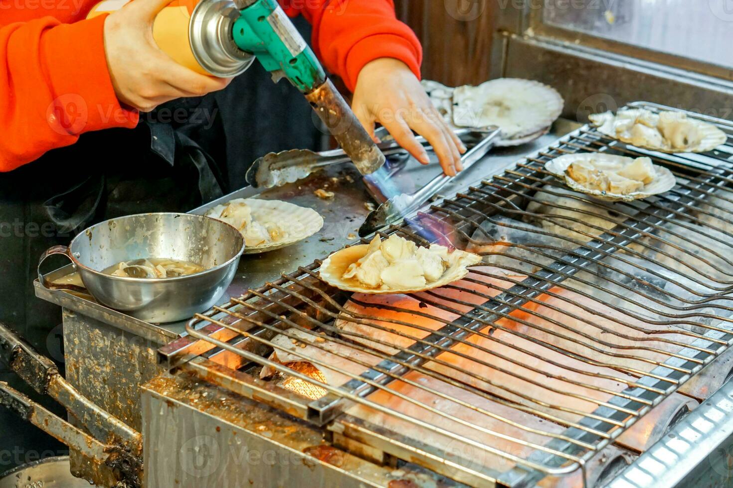 Hand of chef using burner cooking and burn big scallops shells with cheese on stove to sale for customer at Kuromon market. scallops Bar-B-Q is popular among tourists who come to the Osaka, Japan. photo