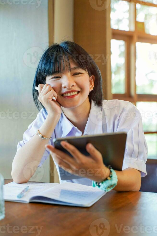 Closeup and front view of happiness cheerful Thai girl student holding a tablet with studying in the classroom on sun flare background. Network education concept. photo
