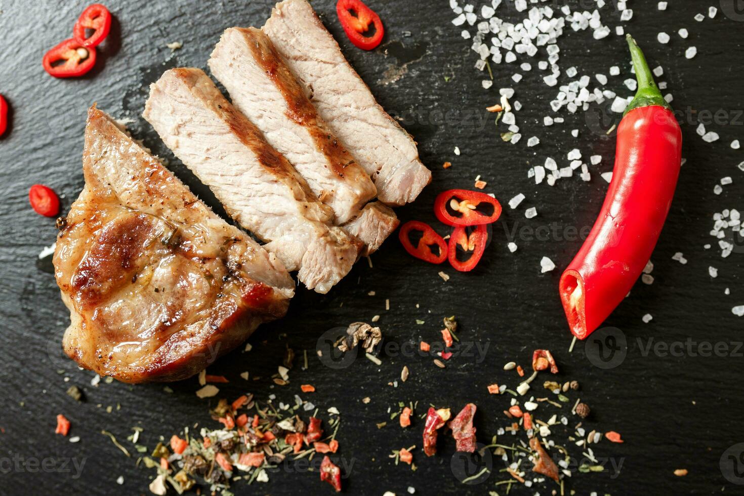 pork cooked in a pan and cut into pieces with spices on a dark stone background photo