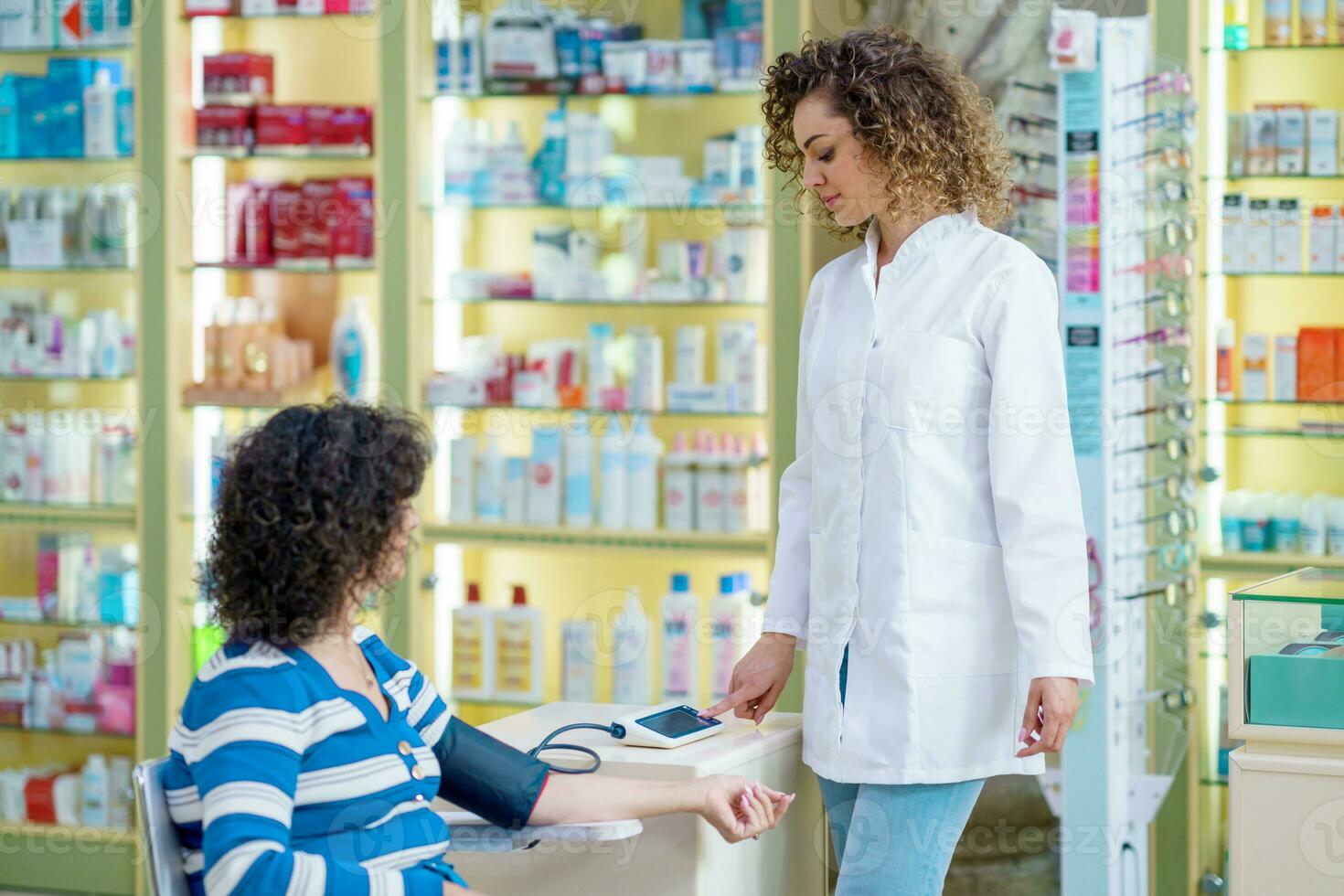 Young woman pharmacist checking blood pressure of lady customer in pharmacy photo