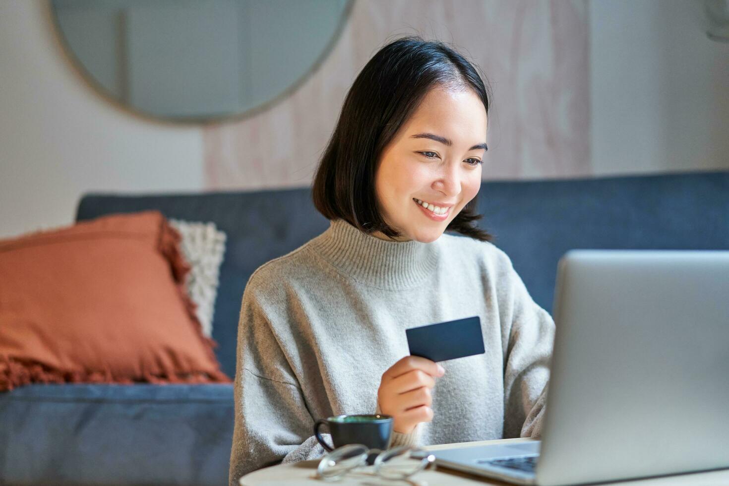 Portrait of korean woman shopping online, using her credit card and laptop to order delivery from website photo