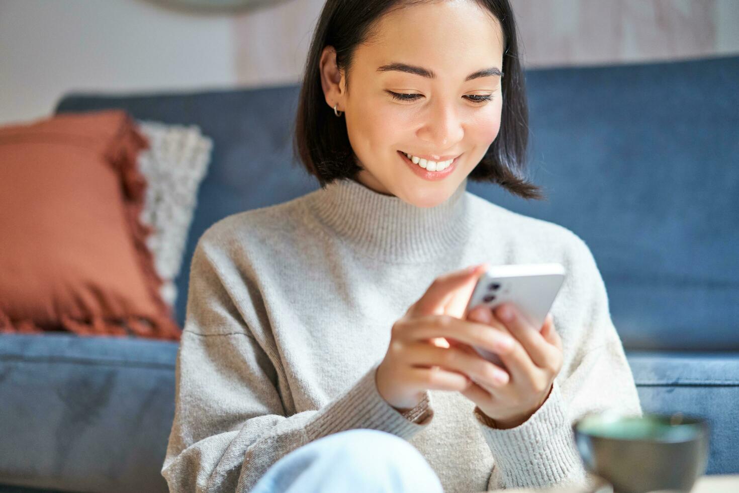 tecnología y gente. joven elegante asiático mujer se sienta a hogar con su teléfono inteligente, mensajes de texto mensaje, utilizando solicitud en móvil teléfono foto