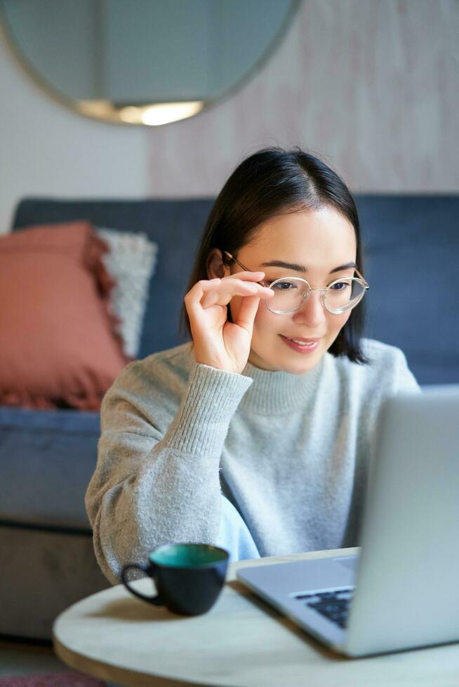 Young asian girl, freelancer professional sitting in living room and working with computer, studying at home using computer photo