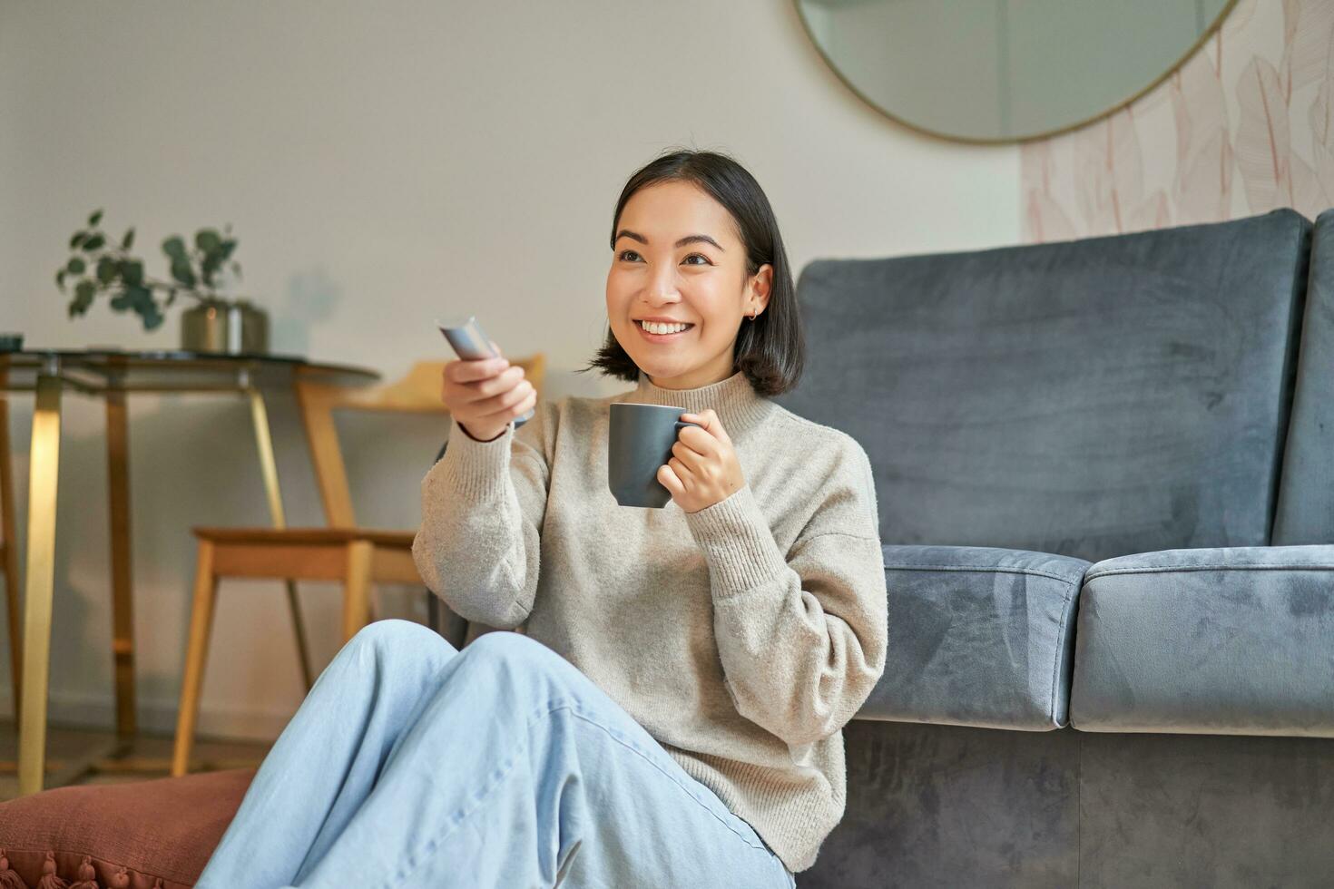 Portrait of young korean woman watching television, holding remote and looking amazed at tv screen, spending time at home photo