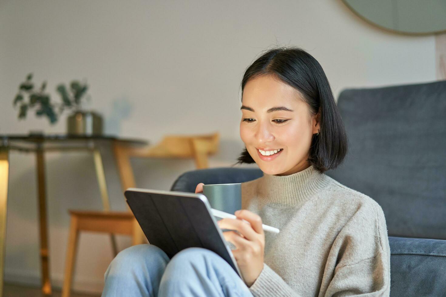 Smiling korean woman sitting with tablet and pen, drawing and scatching her new project or design, working from home photo