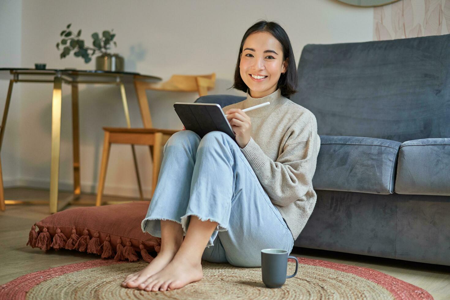 Portrait of creative young woman drawing on digital tablet with pen, drinking coffee, working from home, plan and design new project photo