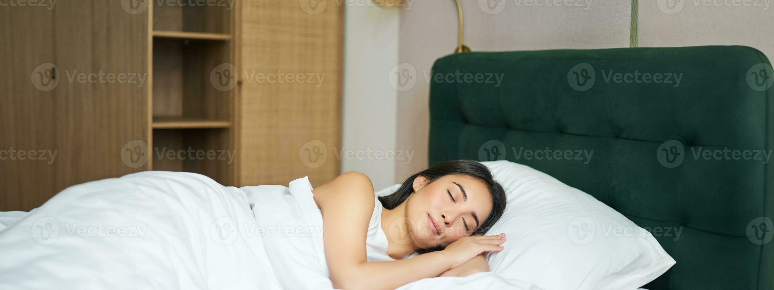 hermosa asiático niña dormido en su cama, acostado en dormitorio con cerrado ojos debajo blanco hojas, calentar invierno funda Nordica foto