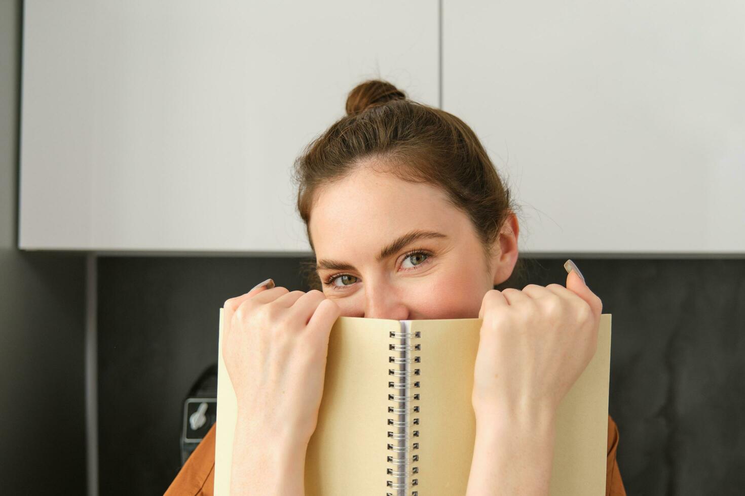 retrato de joven moderno mujer, 25 años viejo, en pie en el cocina con computadora portátil, leyendo notas, estudiante revisando para examen foto