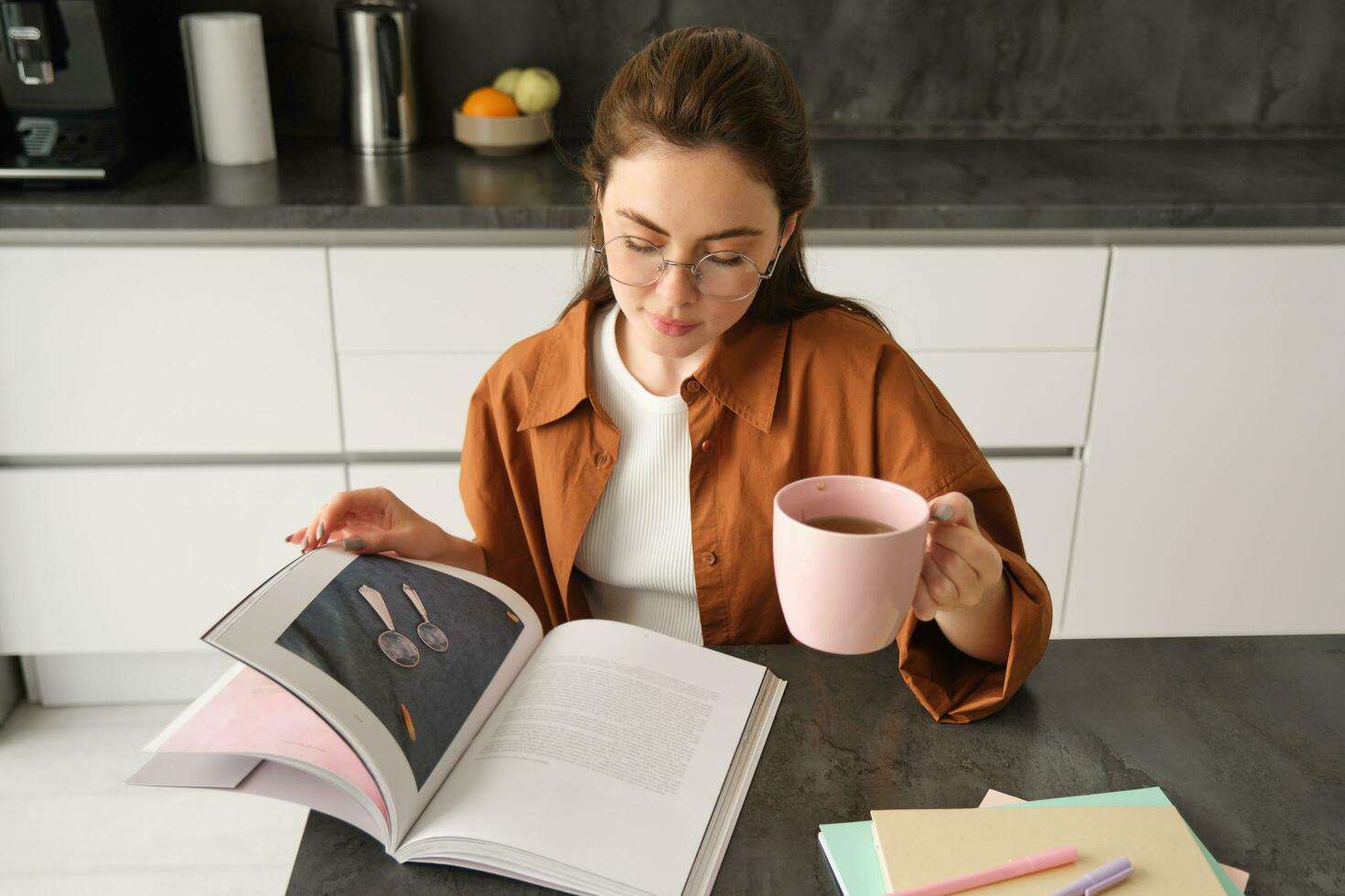 Distance learning. Young woman at home, student studying at home and drinking tea, reading her work book, revising for exam photo