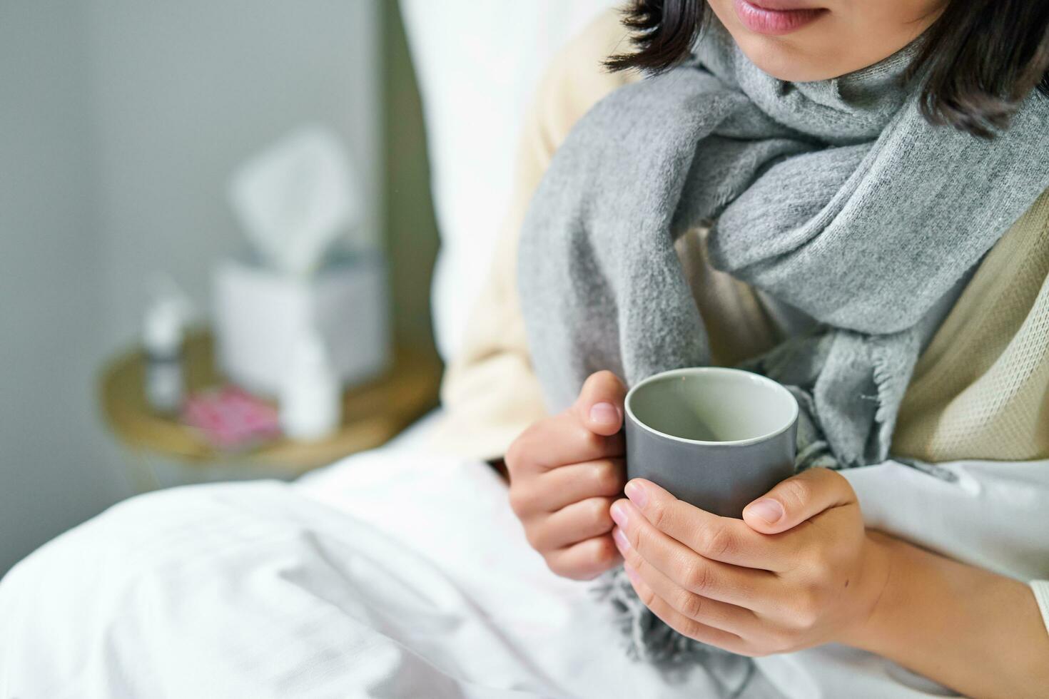 Close up of female hands holding hot drink, lying in bed, girl catching a cold and staying at home photo