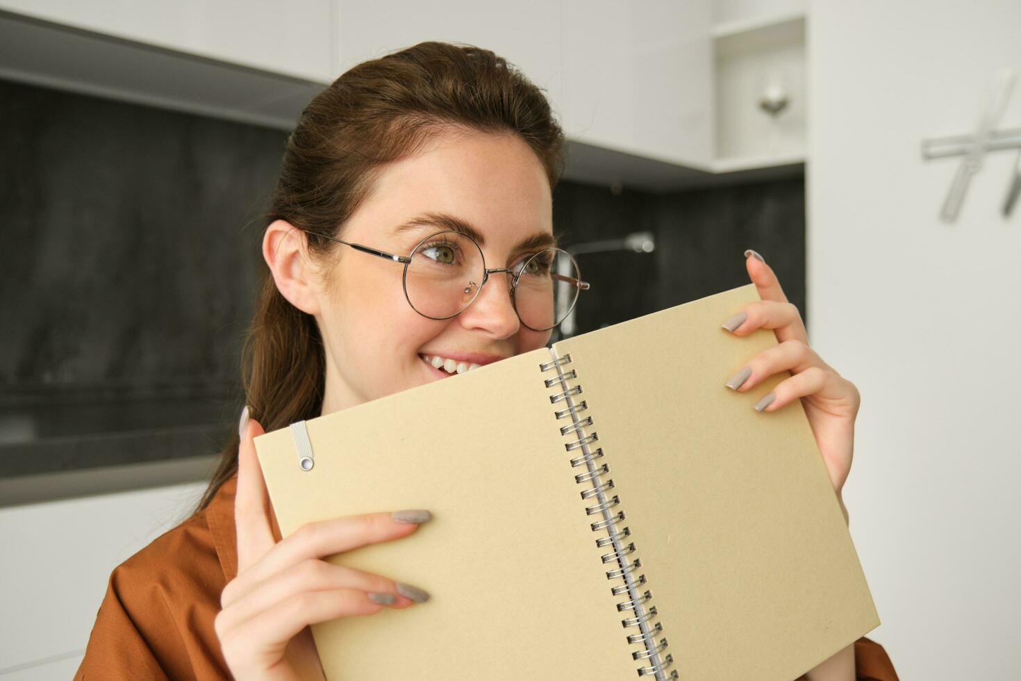Portrait of beautiful young woman studying, student revising at home, doing homework, holding planner, reading her notes and smiling, writing in diary photo