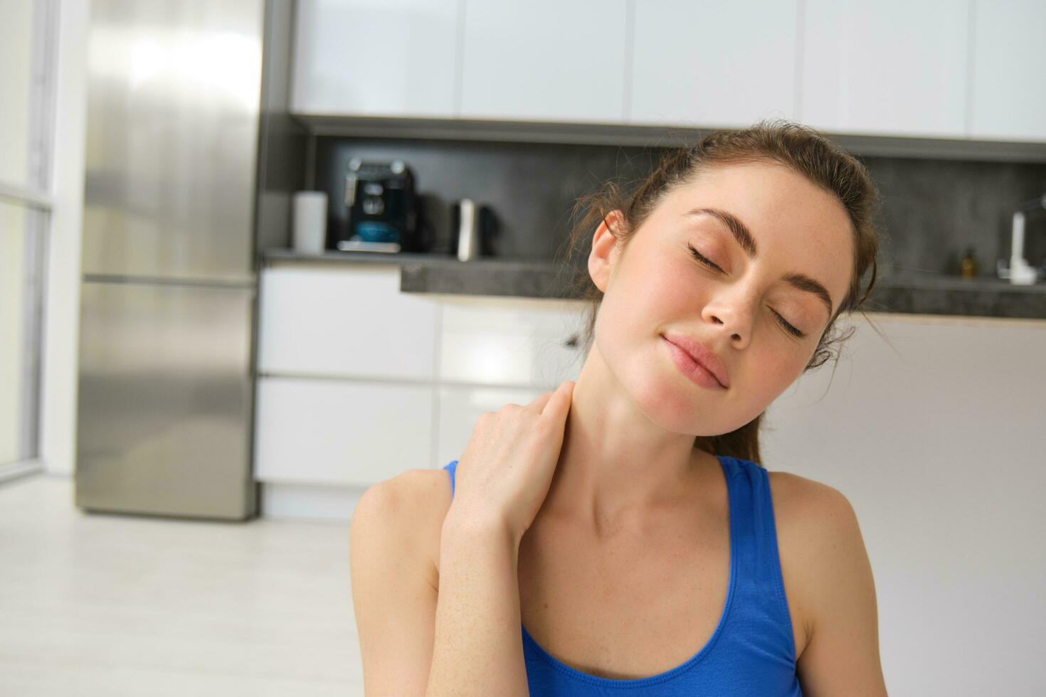 Close-up potrait of fitness woman, does training, workout from home, massaging neck, exercise in living room photo