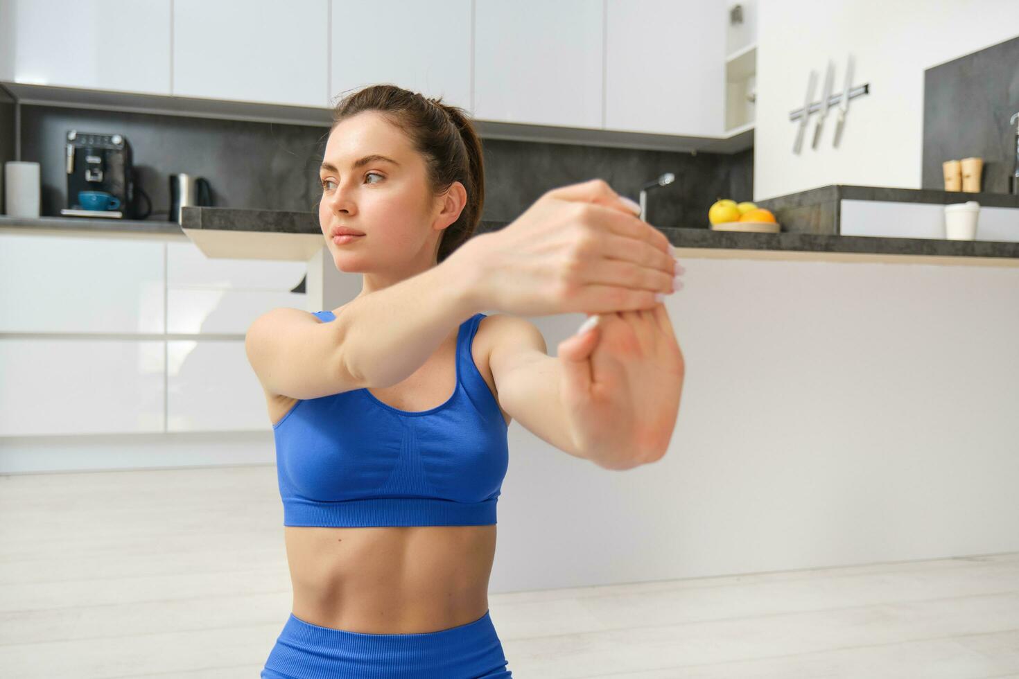 retrato de hermosa mujer lo hace aptitud capacitación, se sienta en piso cerca cocina, extensión su manos, rutina de ejercicio desde hogar foto