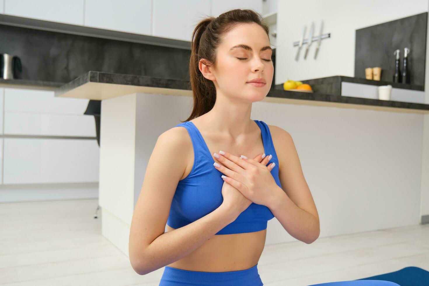 Woman practicing yoga and meditation at home sitting in lotus pose on yoga mat, relaxed with closed eyes. Mindful meditation concept. Wellbeing photo