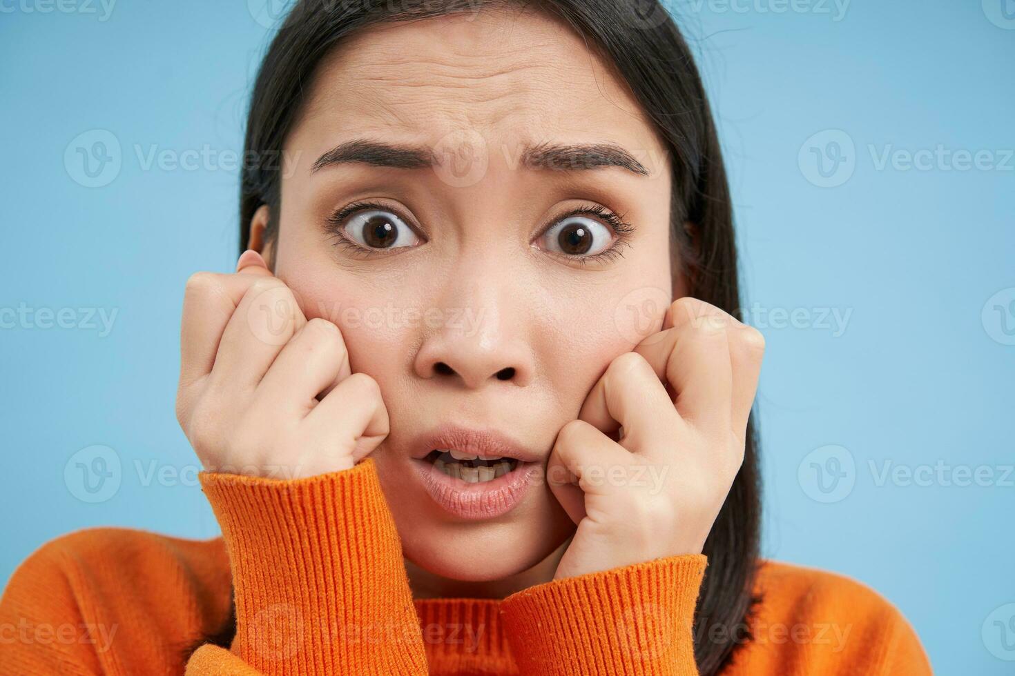 Portrait of scared, anxious young asian woman, looks horrified, stands over blue studio background photo