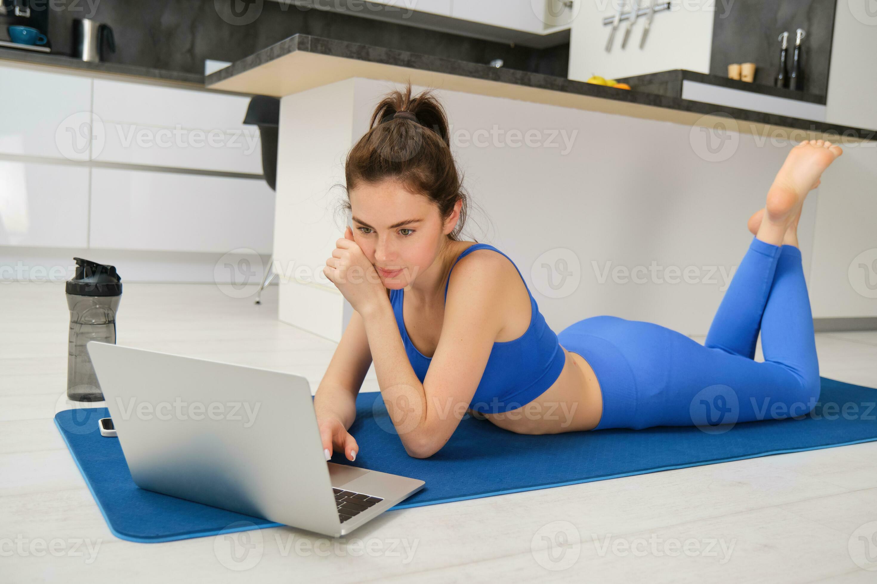 Fit woman doing yoga exercise while watching tutorial on laptop at