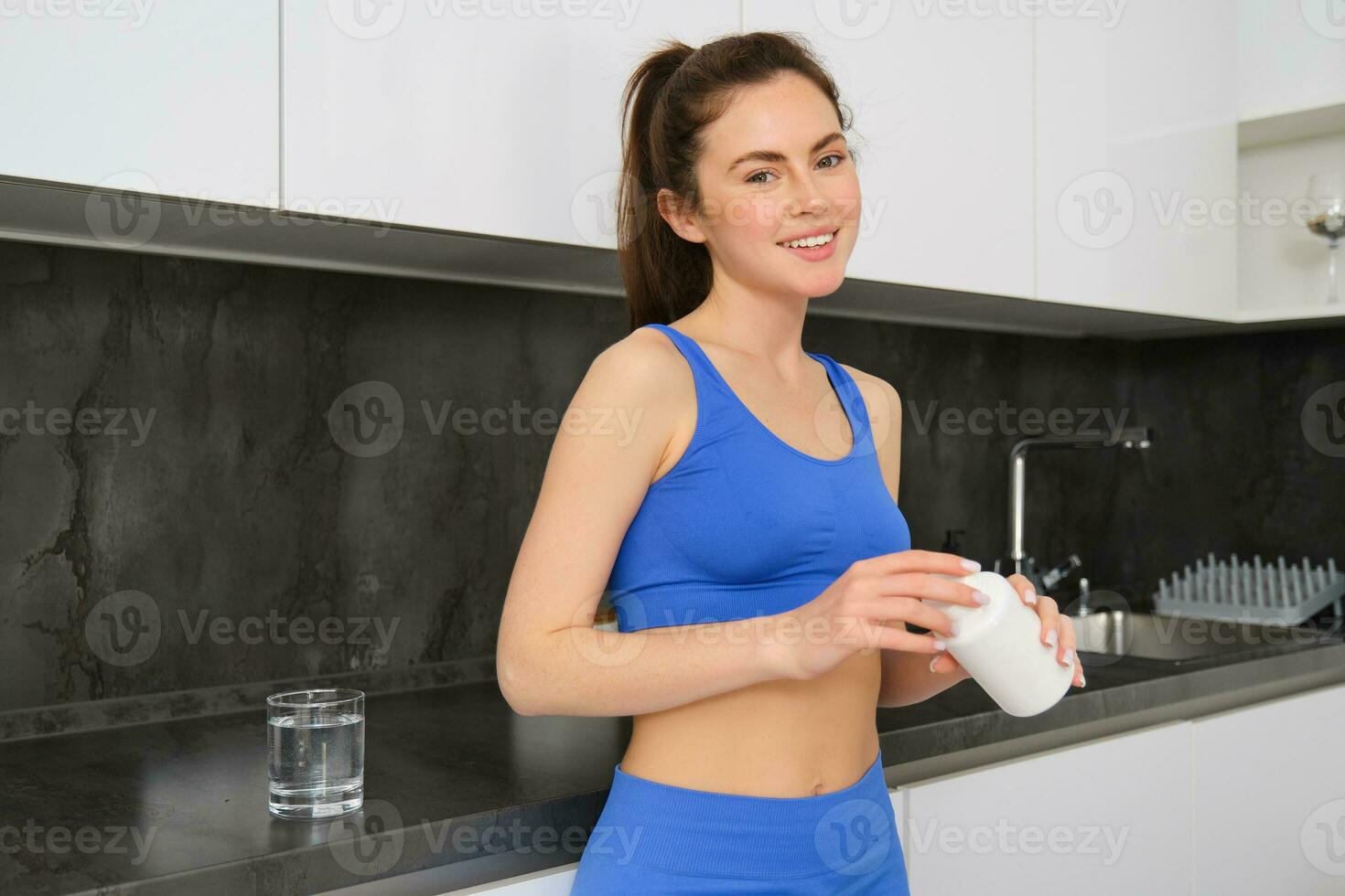 Image of fitness girl, opening bottle of dietary supplement, taking vitamins to stay healthy and fit photo