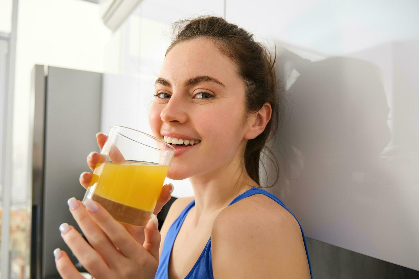 Portrait of smiling brunette sportswoman, drinking fresh juice, detox drink, enjoys freshly squeezed beverage after workout training session photo