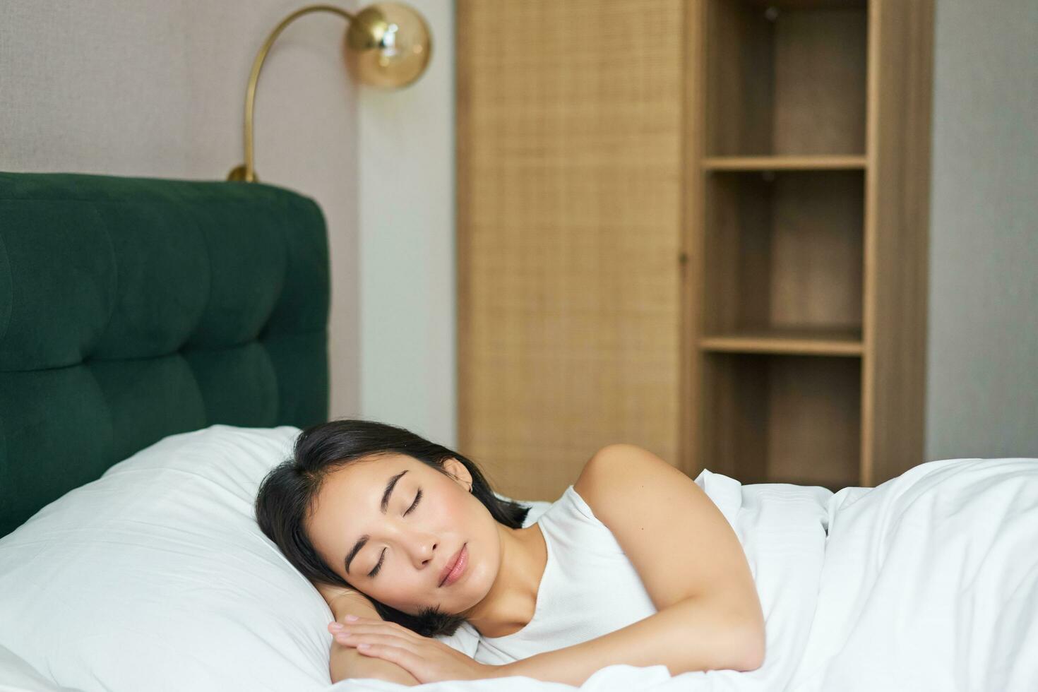 Beautiful asian girl sleeping in her bed, lying in bedroom with closed eyes under white sheets, warm winter duvet photo