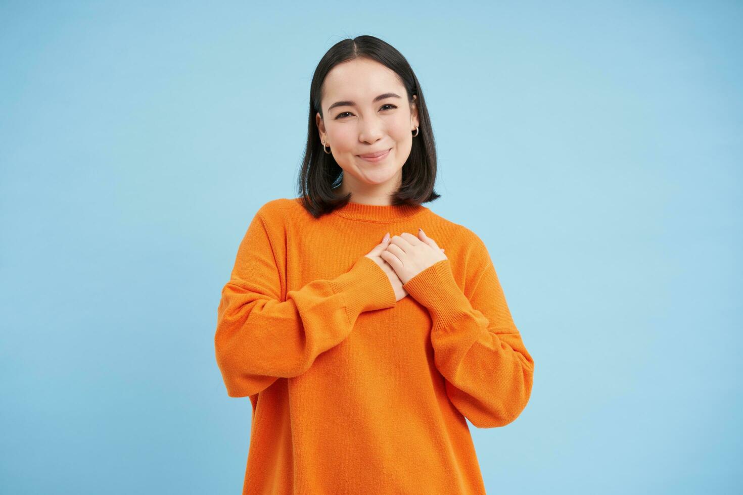 Beauty and skincare. Close up portrait of happy smiling japanese woman, touches her clear, glowing skin, natural healthy face, standing over blue background photo