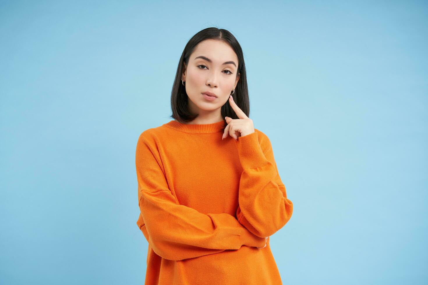 Beauty and skincare. Close up portrait of happy smiling japanese woman, touches her clear, glowing skin, natural healthy face, standing over blue background photo