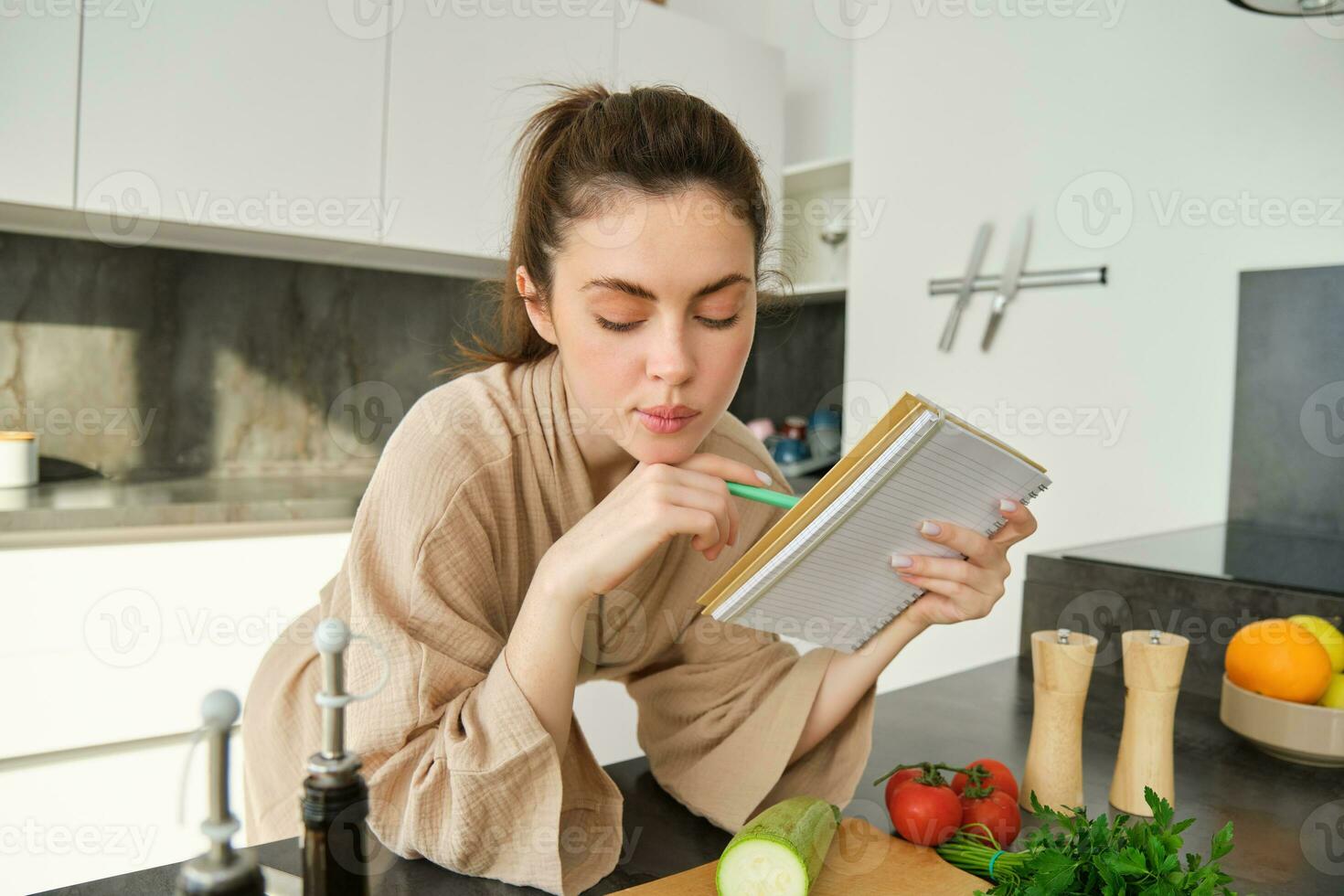 Portrait of modern young woman cooking, making grocery list, reading recipe and making meal, salad in the kitchen, looking at vegetables on chopping board photo