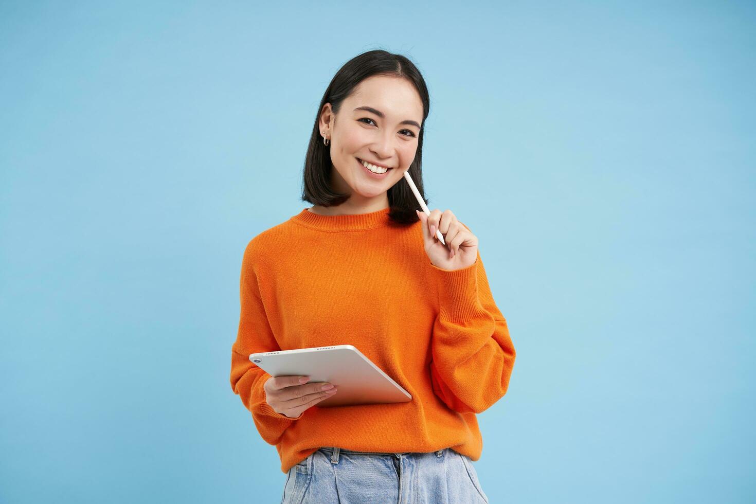 Beauty and skincare. Close up portrait of happy smiling japanese woman, touches her clear, glowing skin, natural healthy face, standing over blue background photo