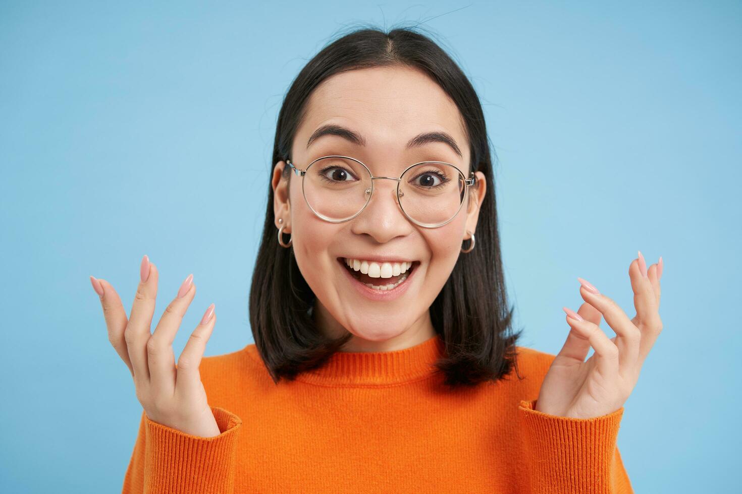 Beauty and skincare. Close up portrait of happy smiling japanese woman, touches her clear, glowing skin, natural healthy face, standing over blue background photo