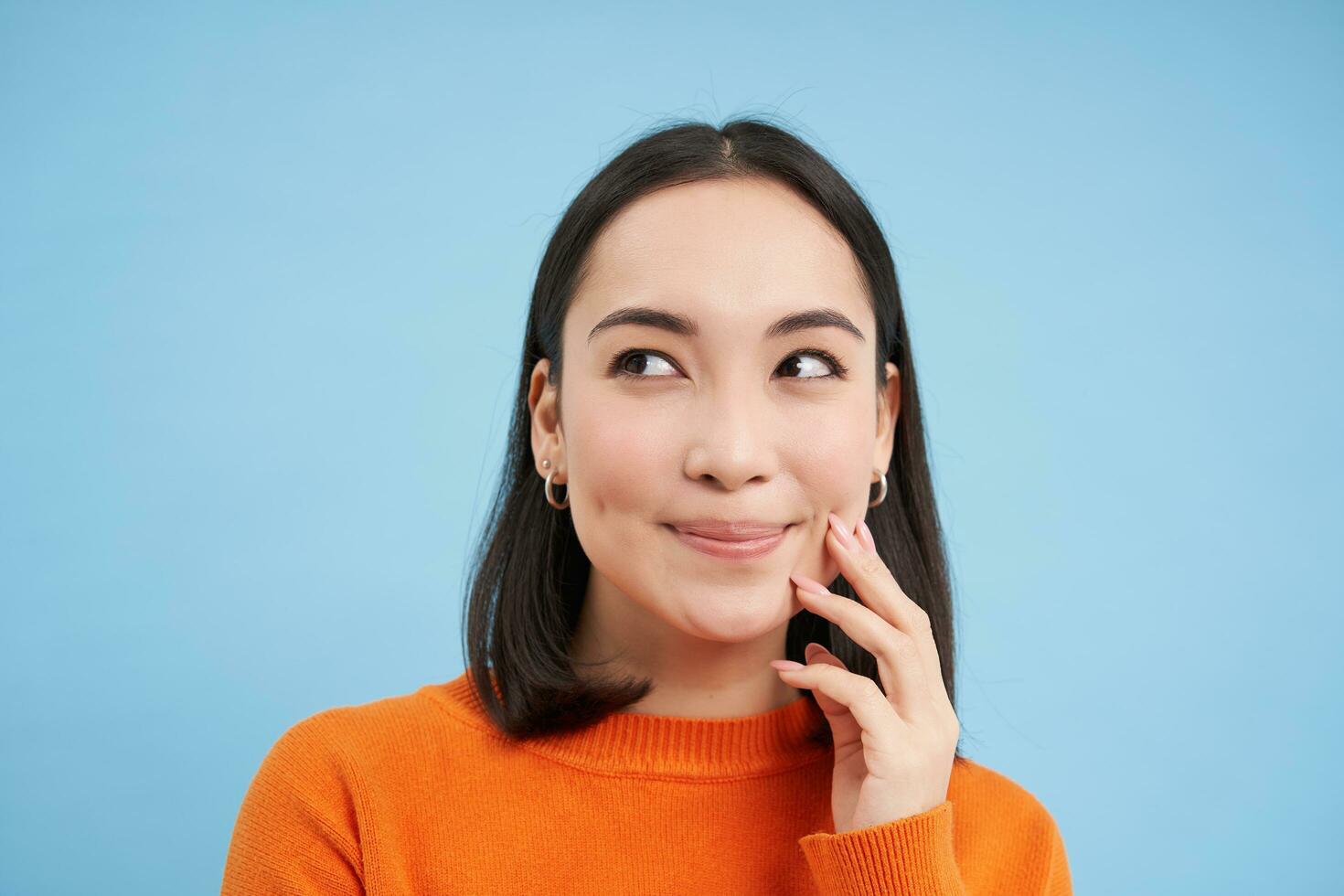 Close up of thinking smiling woman, looking with pleased face at left side copy space, stands over blue background photo