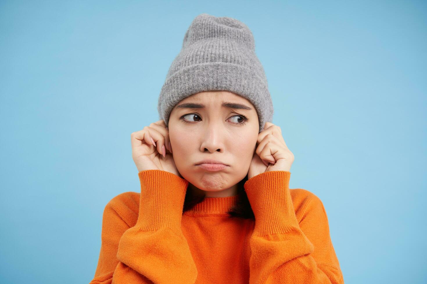 cerca arriba retrato de coreano niña siente frío, batidos y se congela, pone en gorro y se enfurruña con triste rostro, soportes terminado azul antecedentes foto