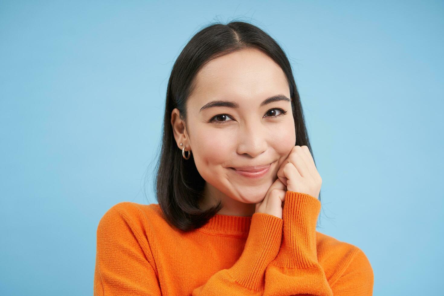 cerca arriba de sincero joven hembra modelo se ríe y sonrisas, muestra natural contento emociones, soportes terminado azul antecedentes foto