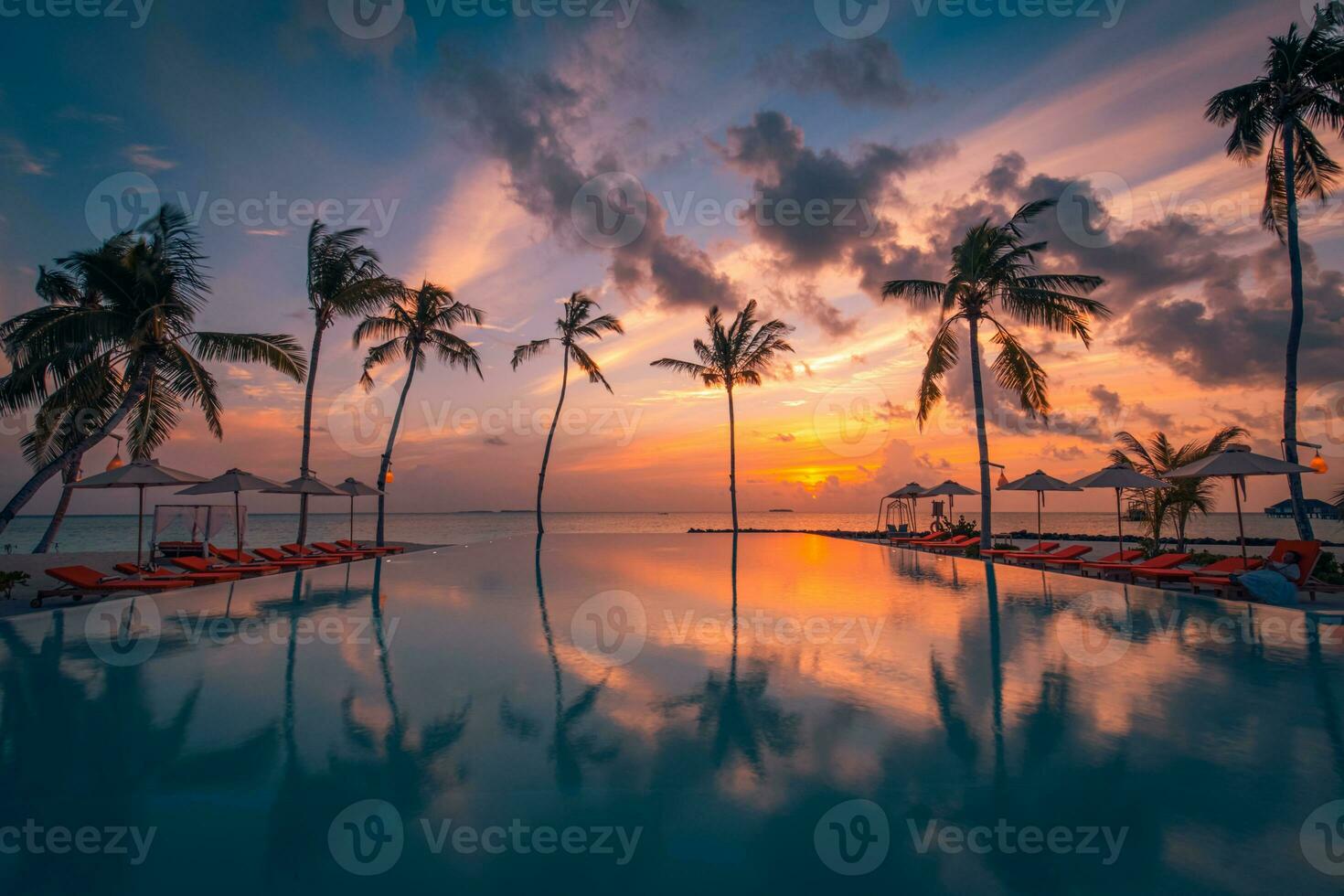 Tropical sunset over outdoor infinity pool in summer seaside resort, beach landscape. Luxury tranquil beach holiday, poolside reflection, relaxing chaise lounge romantic colorful sky, chairs umbrella photo