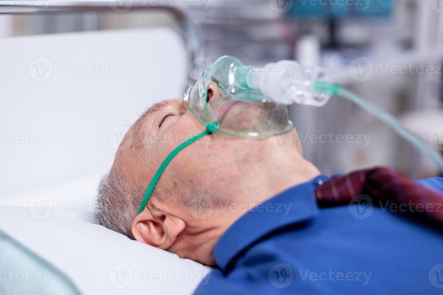 Old male patient weating oxygen mask laying in hospital bed while getting treatment after being infectetd with coronavirus. Medicine medical healthcare system epidemic lungs infection treatment photo