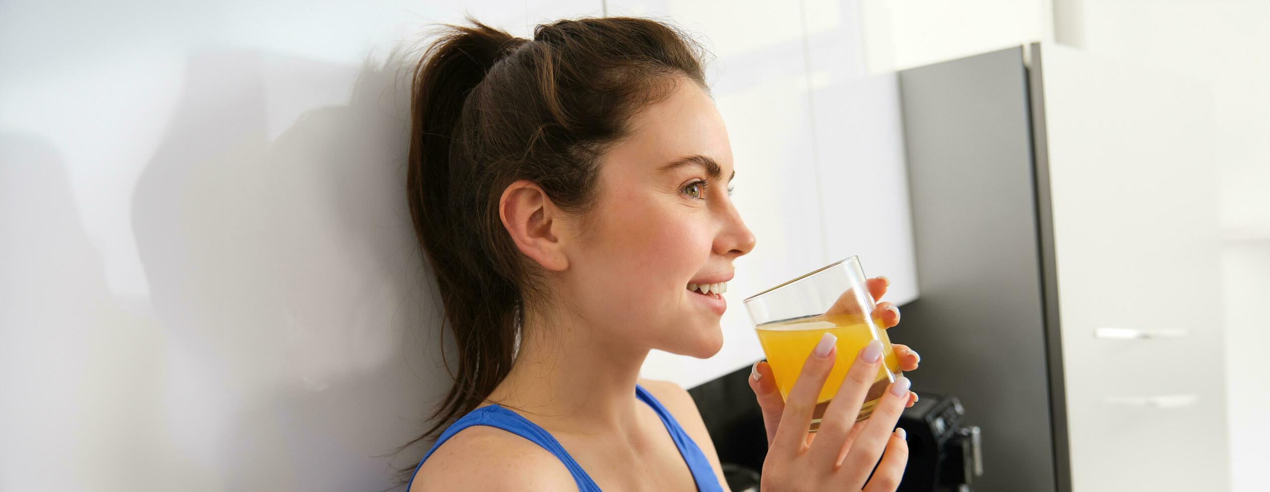 Shot of sporty beautiful woman drinking detox juice in the kitchen at home photo