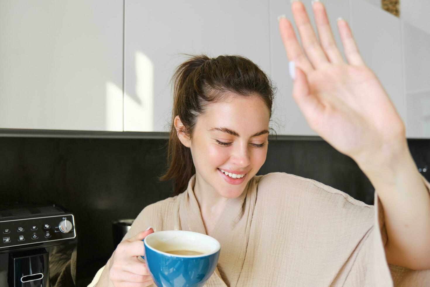 Portrait of beautiful girlfriend covers her face from camera and giggles, holding cup of coffee, concept of romantic mornings at home photo