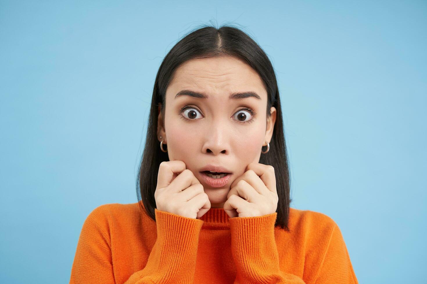 Close up of shocked, scared brunette girl, looking frightened and terrified, standing over blue background photo