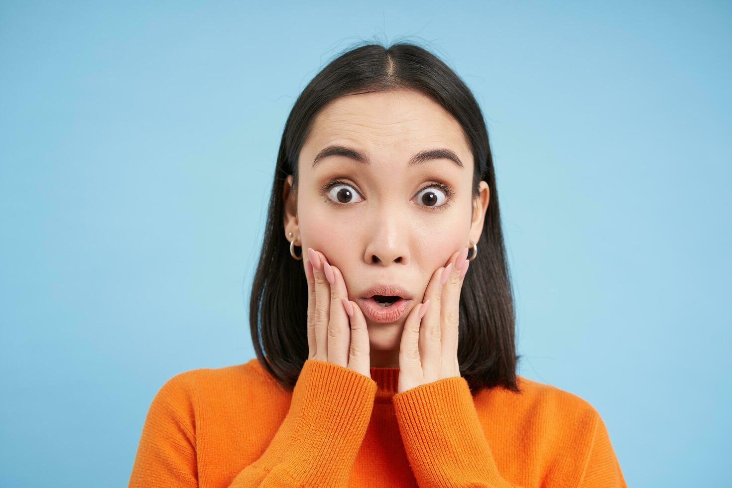 cerca arriba retrato de asombrado morena niña dice Guau, asombrado por algo asiático mujer mira sorprendido a cámara, impresionado reacción, azul antecedentes foto