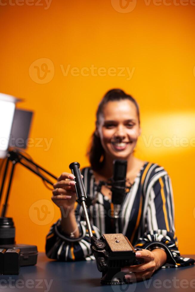 Close up of fluid head of tripod and filmmaker talking about it during vlog. Social media star making online internet content about video equipment for web subscribers and distribution, film photo