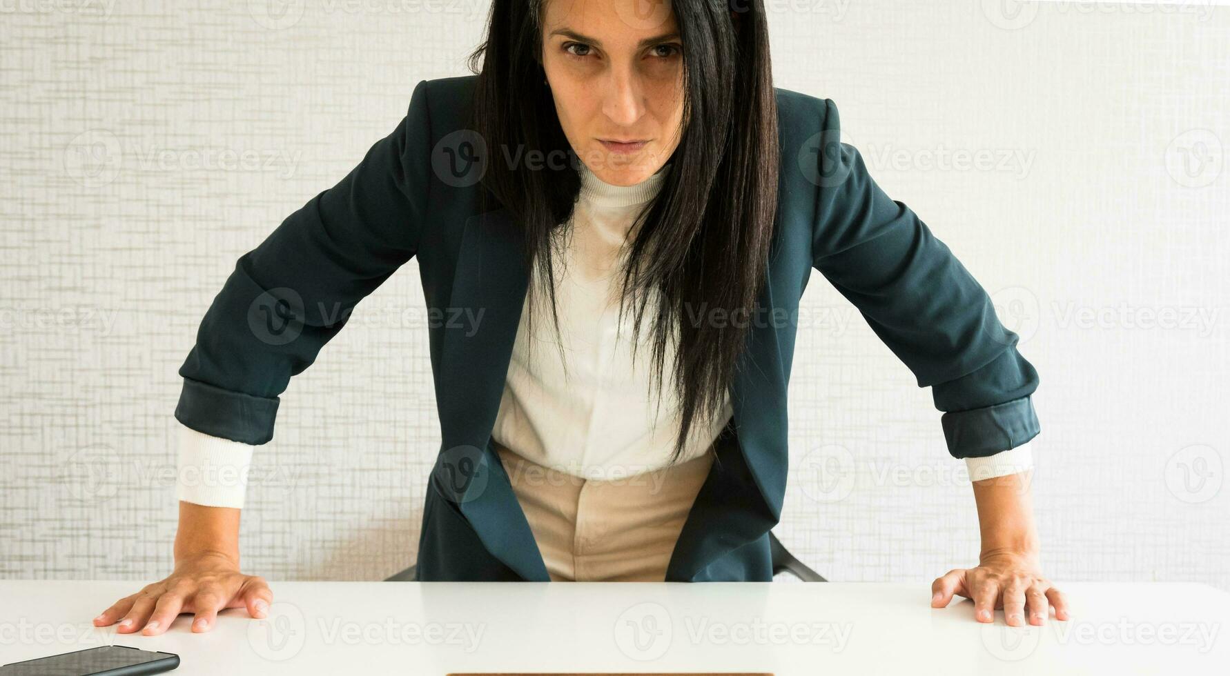 Young caucasian brunette business woman director in office stand up angry face show pressure look at camera pov. Angry director in office raging from seat at you point of view photo