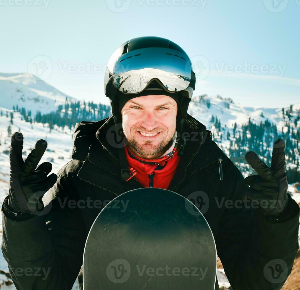 Caucasian snowboarder man wearing ski goggles and colorful ski equipment, showing thumbs up on slope photo
