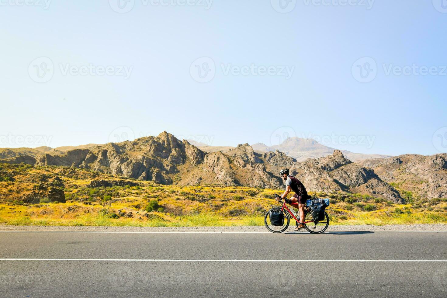 Side view caucasian male cyclist bicycle touring on flat asphalt in caucasus mountains. Active inspirational lifestyle concept. Carefree cyclist lifestyle. Cycle around the world photo