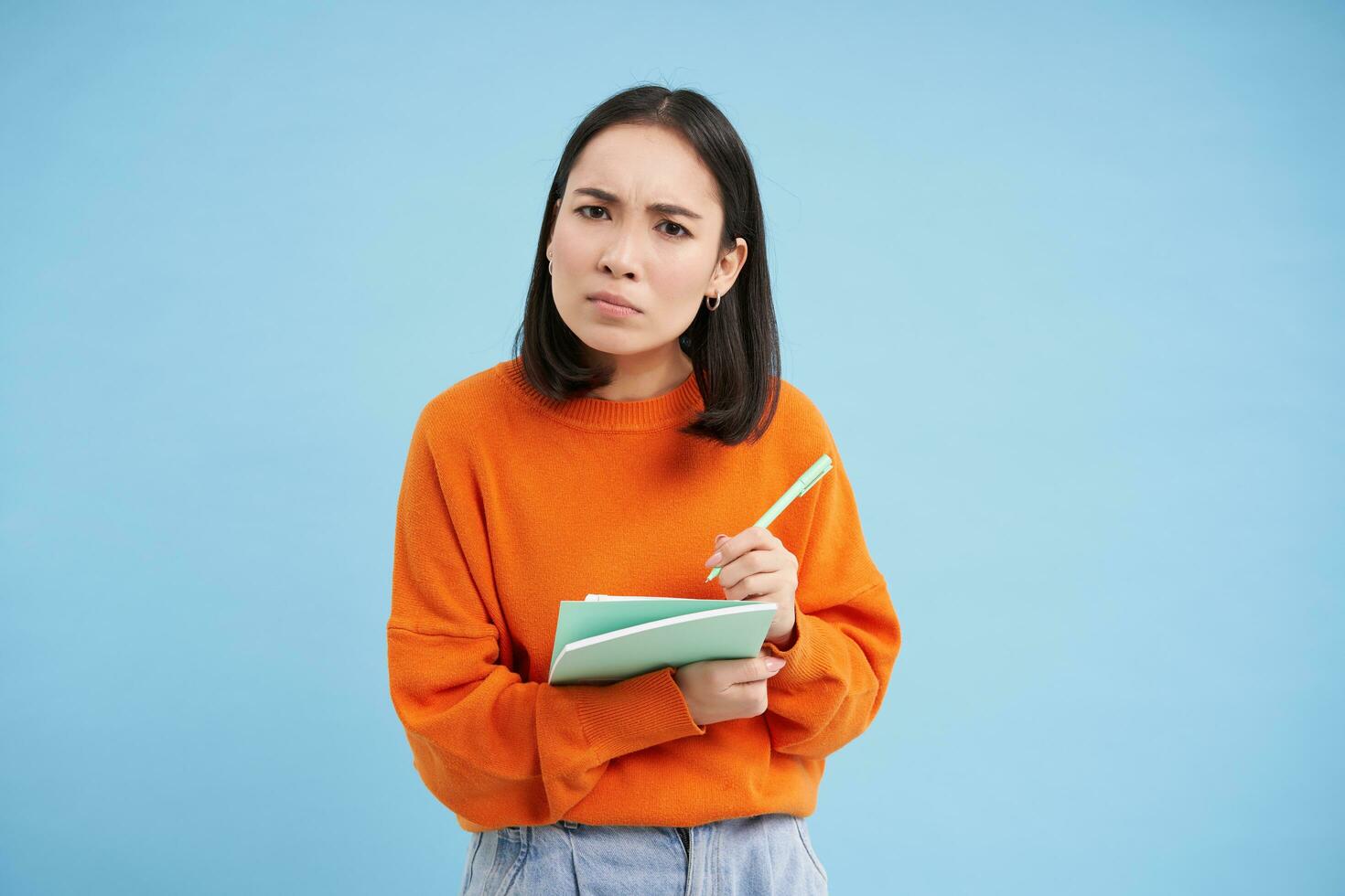 Education and students. Happy asian woman, holding notebooks and laughing, smiling at camera, enjoys going to University or College, blue background photo