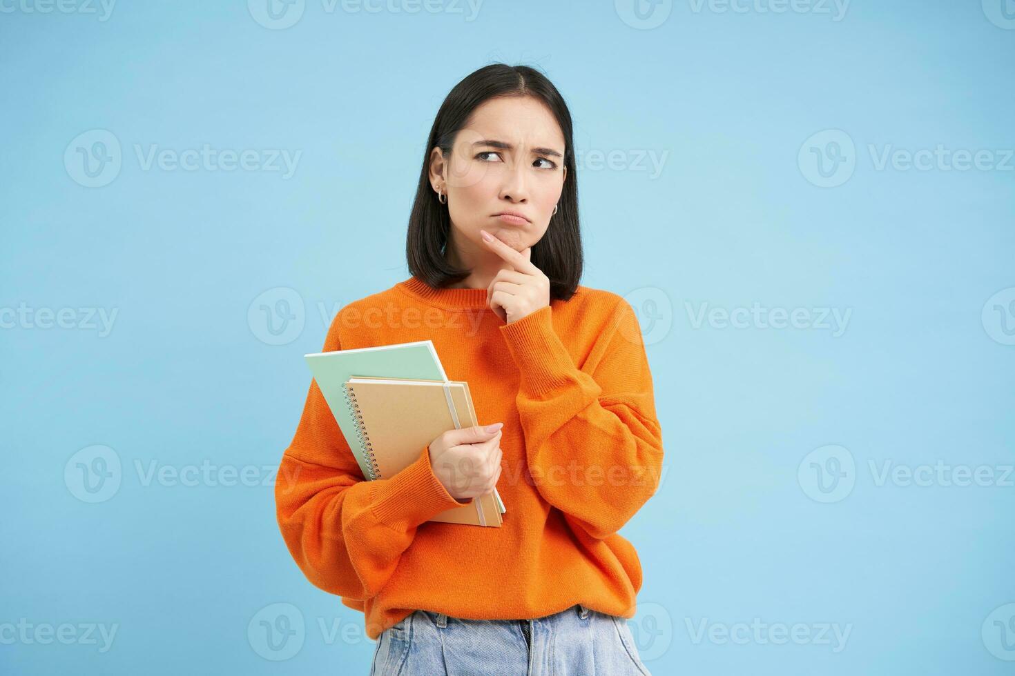 Thinking girl, student with notebooks, stands over blue background thoughtful, making decision photo