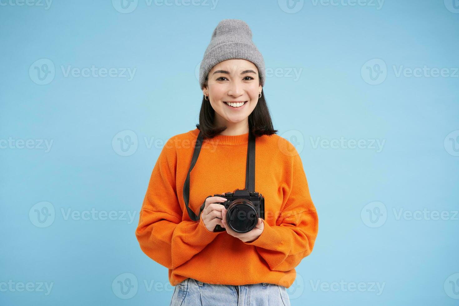 elegante asiático niña con digital cámara, tomando fotos. mujer fotógrafo sonriente, en pie terminado azul antecedentes foto