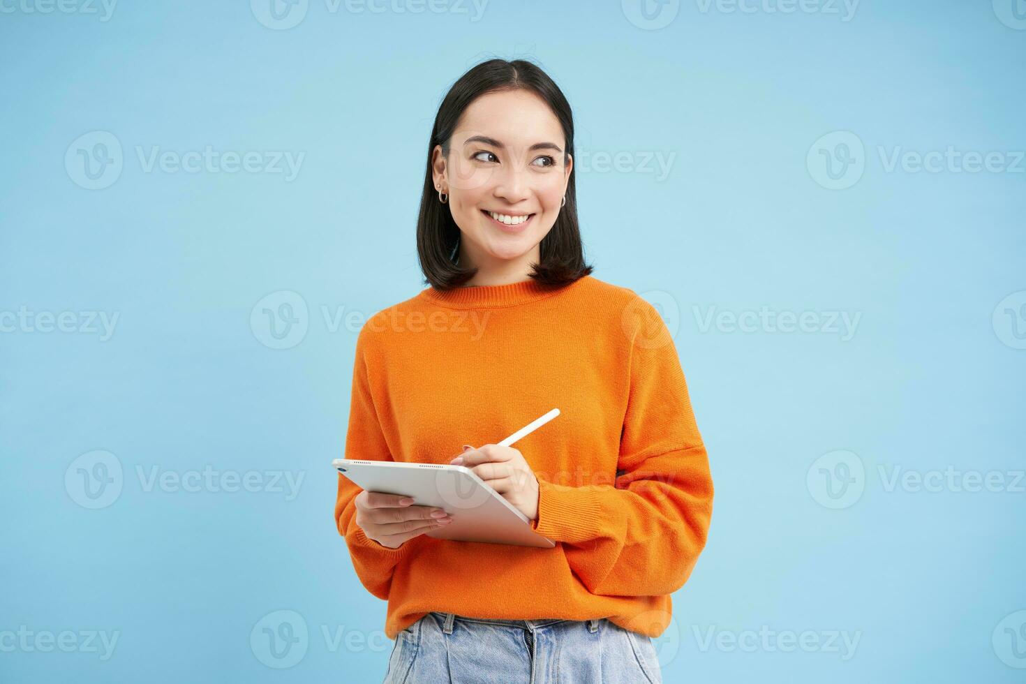 Portrait of young Chinese woman, teacher or student with digital tablet and pencil, writing, taking notes, doing her homework, standing over blue background photo